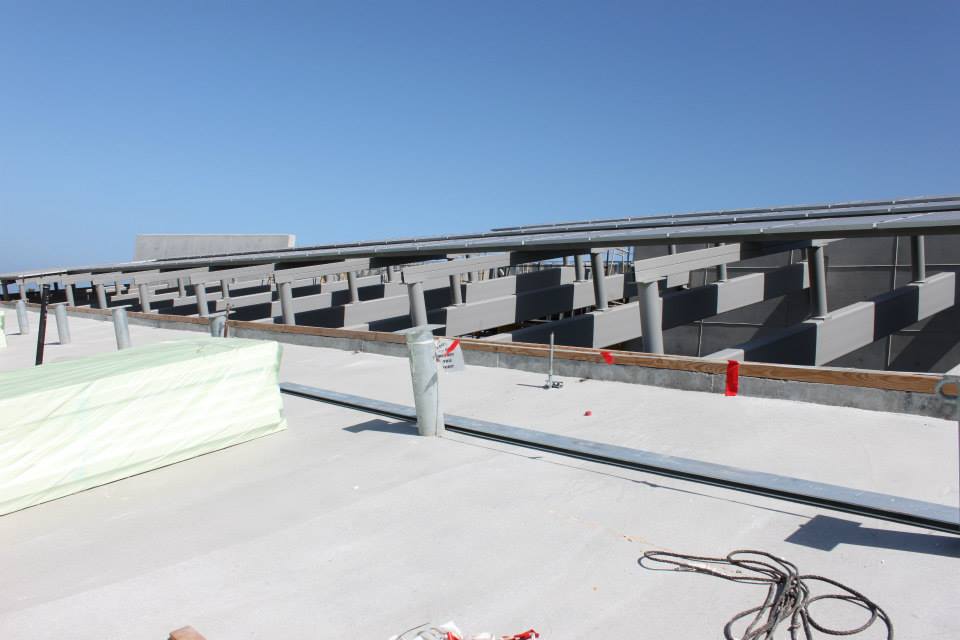 Rows of metal framework structures on a flat rooftop under clear blue sky, with some construction materials and cables visible in the foreground.